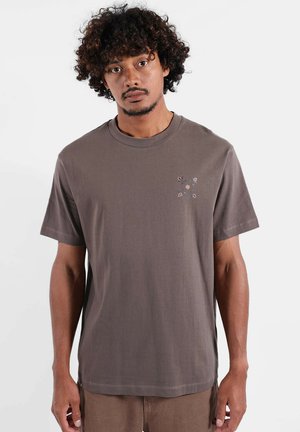 T-shirt en coton marron à manches courtes, avec un petit motif floral sur la partie gauche de la poitrine. Coupe souple et décontractée avec un col rond.