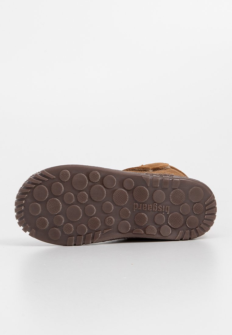 Braune Wildlederschuhe mit einer strukturierten Gummisohle, die kreisförmige Muster aufweist. Die Sohle ist dunkelbraun, und der Schuh hat ein schlichtes Design ohne Hardware.