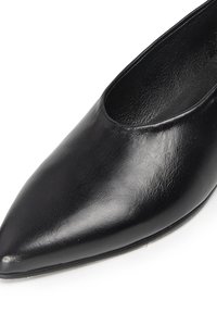 Zapato de cuero negro con punta afilada, de textura suave y diseño semi-abierto en la parte superior. La suela es plana y ligeramente redondeada en la parte delantera.