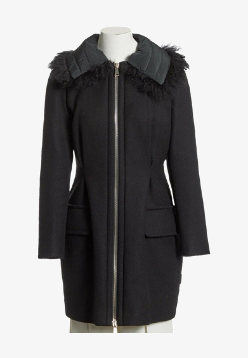 Manteau noir longueur genou avec fermeture éclair à l’avant, grand col matelassé et bordure en fourrure texturée aux épaules, exposé sur un mannequin blanc.