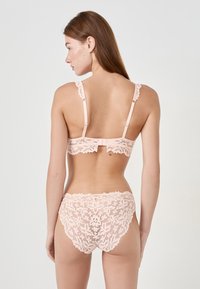 Zestaw koronkowej bielizny w jasnoróżowym kolorze, z delikatnymi wzorami kwiatowymi, regulowanymi ramiączkami i zapięciem z tyłu. Z wykończeniem w postaci akcentujących brzegów.