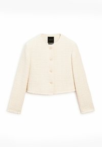 Veste courte texturée crème à manches longues, col rond et quatre boutons à l'avant, étiquette visible à l'intérieur du col.
