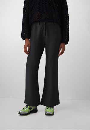 Black wide-leg trousers made from a smooth, matte material, paired with a black open-knit sweater and neon-accented sneakers.