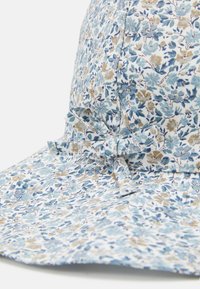 Blomsterprintet bøttehat i lyseblå, hvid og beige bomuldsstof. Har en hage-rem, der er bundet som en sløjfe. Blød tekstur, bred skygge.
