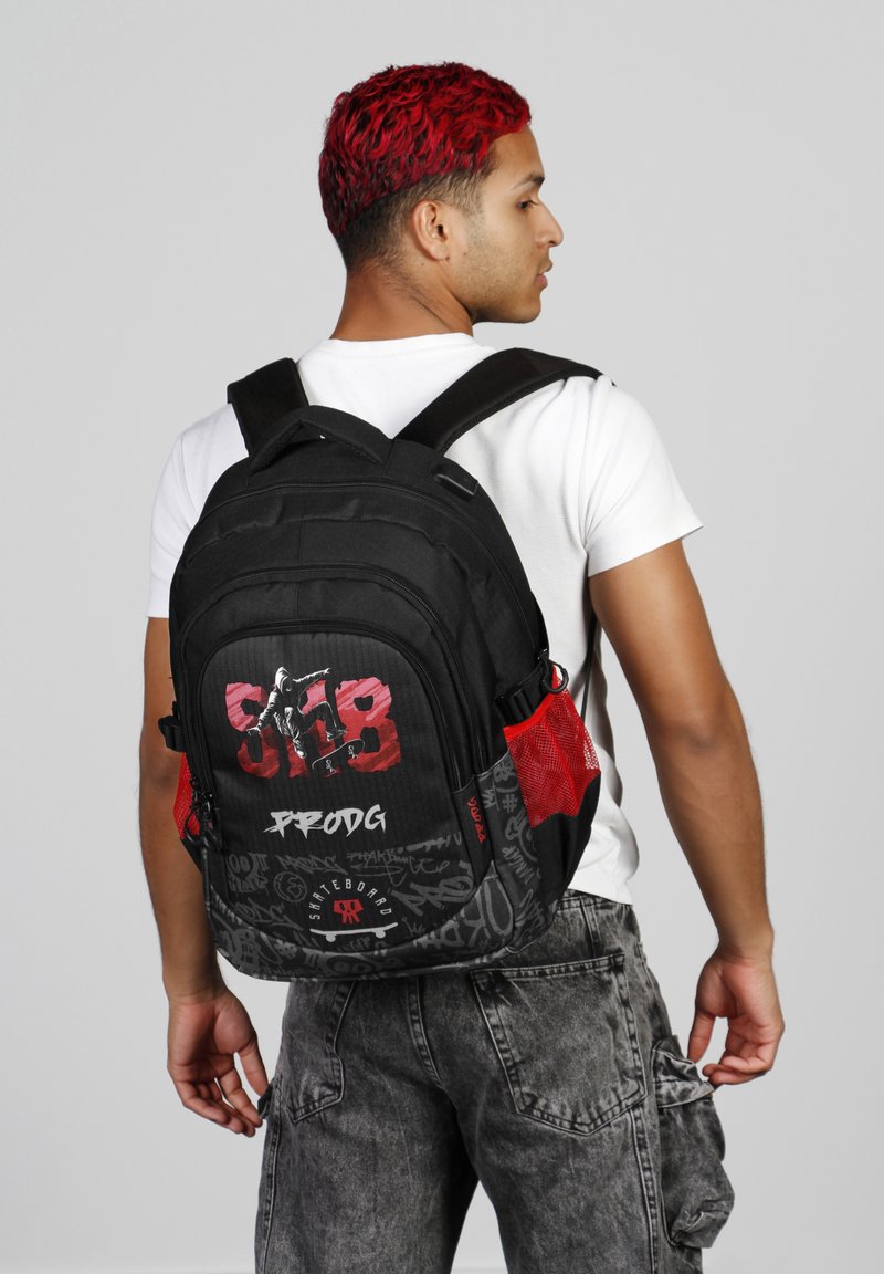 Mochila negra con acentos de malla roja y un diseño gráfico que presenta imágenes de monopatines y texto. Correas ajustables, tela resistente y múltiples bolsillos.