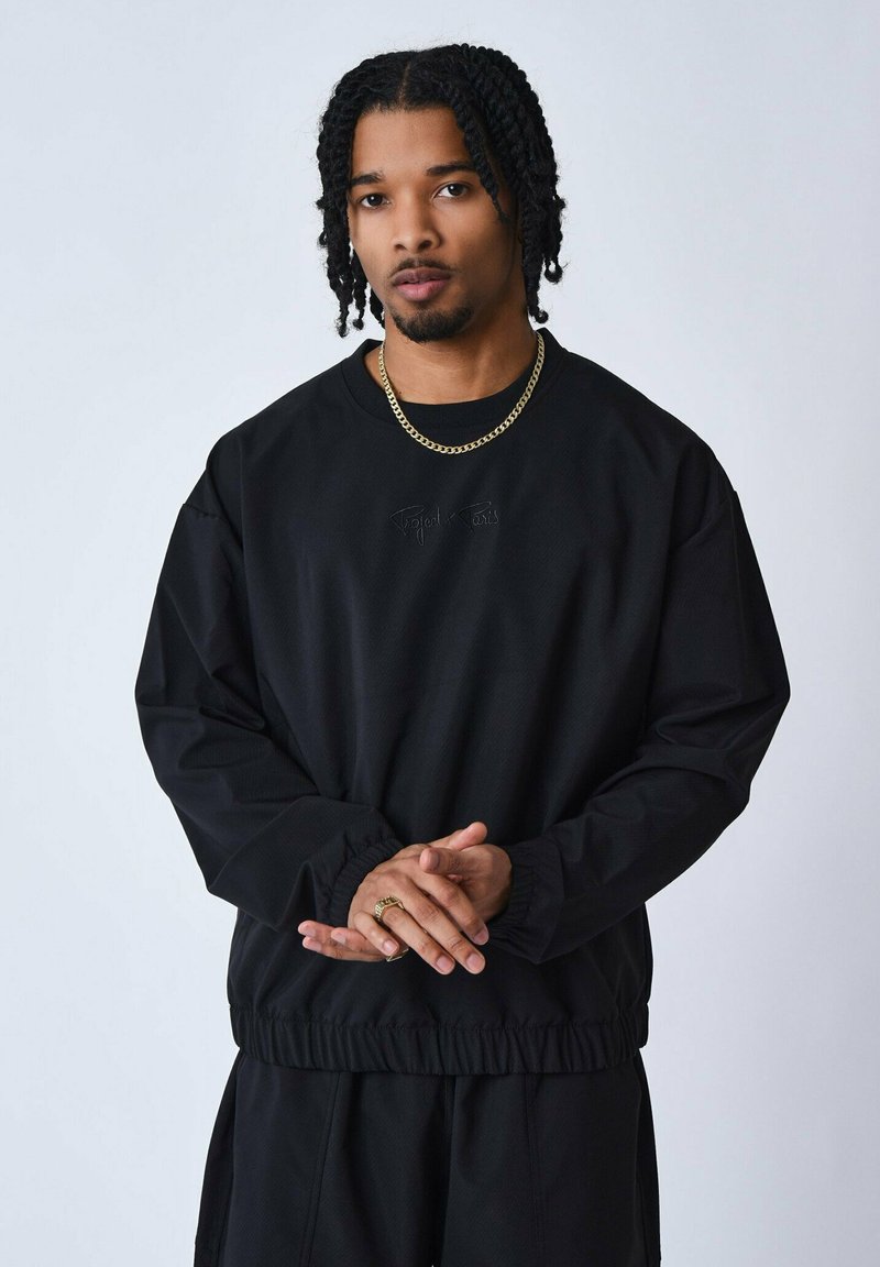 Sudadera negra de manga larga con puños y dobladillo elásticos, que presenta un sutil logotipo en relieve en el centro. Textura suave, ajuste casual.