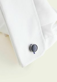 Weißer Hemdmanschette mit strukturiertem Stoff, einem runden blauen Akzentknopf und blauen Nähdetails. Glatte Textur mit einem klaren Design.