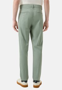 Lichtgroene broek van gladde stof, met een recht model, twee achterzakken en gedragen met witte sneakers.