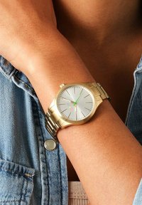 Orologio da polso in oro con quadrante argento, lancetta dei secondi verde e marcatori delle ore. Cinturino a maglie metalliche e design della cassa rotondo.