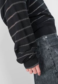 Zwarte gebreide trui met zilveren horizontale strepen en geribde manchetten, gecombineerd met donkergrijze denim jeans met een vervaagde afwerking.
