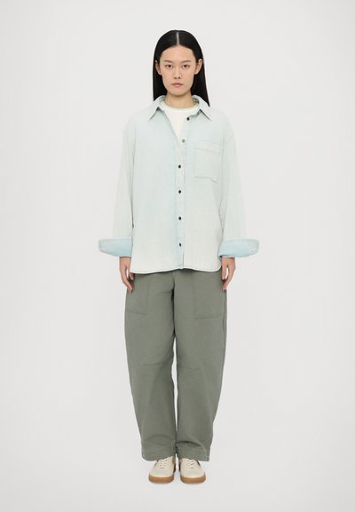 Cămașă din denim de un albastru deschis, cu nasturi și un buzunar pe piept, asortată cu pantaloni largi de culoare verde măslin. Design simplu, croială lejeră și mâneci lungi.