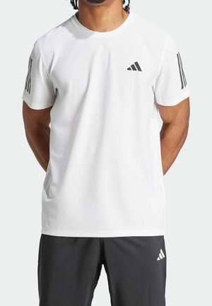 Homme portant un t-shirt blanc Adidas à manches courtes avec des bandes noires sur les manches et un short de sport noir avec le logo Adidas.