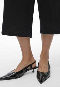 Crne lakirane cipele s remenčićem na petu s oštrim nosom i 3 cm niskim potpeticama, s glatkom završnom obradom i minimalističkim dizajnom.
