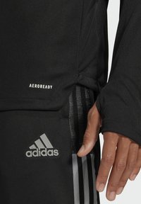 Schwarzes Sportoberteil mit AEROREADY-Logo. Es hat lange Ärmel, eine gerippte Textur und einen Akzent von drei weißen Streifen an der Seite.
