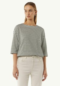 Gestreepte grijs en zwarte T-shirt met korte mouwen, een brede halslijn en een relaxte pasvorm, gecombineerd met lichtgekleurde strakke jeans.