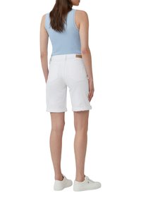 Lichtblauw tanktop met kantafwerking, gecombineerd met witte omslagdenimshorts. Het model draagt witte sneakers, wat een gladde stoftextuur laat zien.