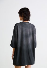 Oversized black t-shirt with a gradient finish, short sleeves, and a round neckline. Features a subtle logo on the upper back.