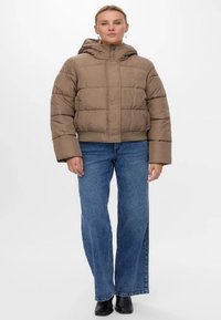 Lyhyt ruskea puhvisetakki hupulla, jossa on laatikkomainen muotoilu ja ommellut paneelit. Yhdistetty vaaleansinisiin leveälahkeisiin farkkuihin.