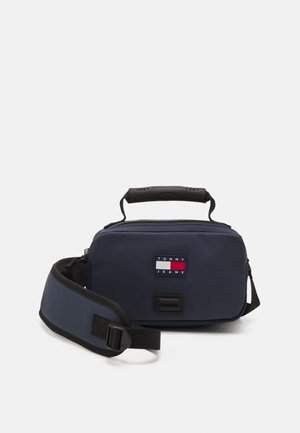 Navy polyester crossbody bag with a black handle, adjustable strap, and front logo patch in red, white, and blue. Zippered main compartment.