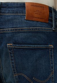 Σκούρο μπλε τζιν από denim με πορτοκαλί ραφές και καφέ δερμάτινο ταμπελάκι με την ένδειξη "Jack & Jones" πάνω από την πίσω τσέπη.