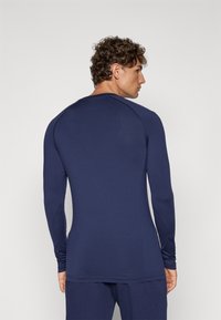 Cămașă navy cu mâneci lungi, realizată dintr-un material neted și elastic. Prezintă un decolteu rotund și un design ajustat, cu detalii fine în cusături.