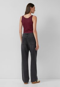 Burgundowa top na ramiączkach z koronkowym wykończeniem, zestawiony z wysokim stanem ciemnoszarymi spodniami typu wide-leg. Gładki materiał i minimalizm w detalach.