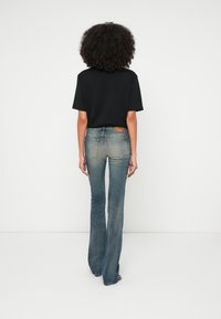 Cămașă neagră cu mâneci scurte, asortată cu blugi evazați de culoare albastru deschis. Blugii au o textură decolorată și un patch pe buzunarul din spate.