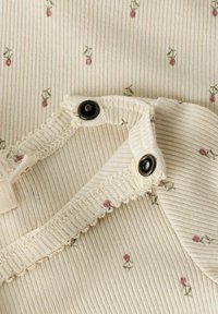 Tissu côtelé crème avec de petits motifs floraux roses et des boutons-pression noirs sur les bords superposés de l'encolure d'un vêtement.