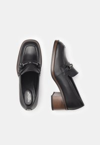 Scarpe in pelle nera con punta quadrata, hardware metallico decorativo e tacco a blocco rigato. Texture liscia e design minimalista.