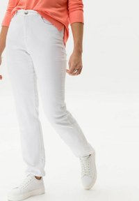 Vaqueros de mezclilla blanca con un ajuste recto, cierre de botón en la parte frontal y dos bolsillos laterales, combinados con zapatillas blancas y una blusa de manga larga color coral.