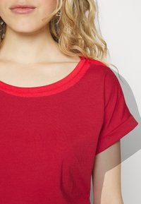 T-shirt di cotone rosso con scollatura rotonda e maniche arrotolate, caratterizzata da una texture liscia e priva di motivi o accessori visibili.