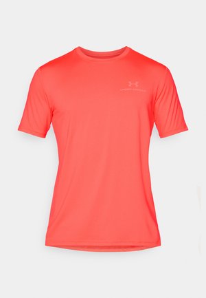 Kortermet, lys korall atletisk skjorte laget av glatt stoff, med rund hals og subtil logo på brystet.