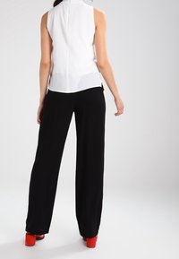 Top blanco sin mangas con cuello alto, combinado con pantalones negros sueltos y zapatos de tacón rojos. Tejido liso, diseño minimalista.