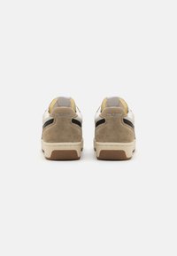 Białe i beżowe sneakersy z zamszowym obcasem, czarnymi akcentami, żółtym wnętrzem i gumową podeszwą. Posiadają minimalne logo na obcasie.