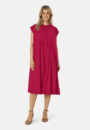 Fuchsia jurkje tot op de knie met kapmouwen, knoopsluiting aan de voorkant en gecentreerde taille, gemaakt van een lichte stof. Draagt met beige hakken.