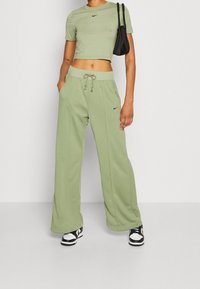 Svetle zelené zkrácené tričko a široké teplákové kalhoty ve stejném odstínu, oboje s malým černým logem Nike. Kombinováno s černobílými teniskami.