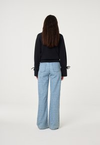 Zwarte cropped top met lange mouwen en trekkoordmanchetten, gecombineerd met lichtblauwe gestreepte wijde broek van denim met achterzakken.