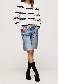 Woman wearing a white and black striped knit cardigan and sweater, knee-length denim skirt, black socks, and black heeled sandals.