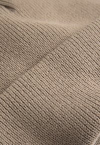 Beige gebreide stof met een textuur en ribbelpatroon. Het materiaal lijkt zacht en flexibel, ideaal voor kleding of huistextiel.
