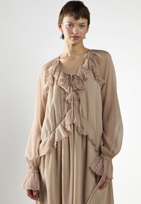 Chiffon-Kleid in Blush-Tönen mit Rüschendetails, langen Ärmeln und Bindeband. Fließendes Design mit geschichteter Textur und gerafften Manschetten.