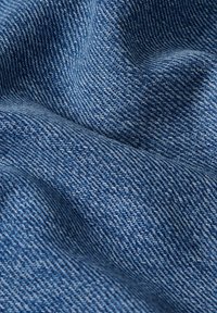 Sinine denim kangas, millel on tekstureeritud pind, nähtavad kootud mustrid ja värvi intensiivsuse kerge varieerumine.