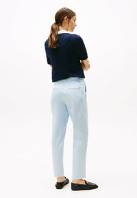 Granatowy sweter w splot kablowy, jasnoniebieskie dopasowane spodnie i czarne buty wsuwane. Prosty design, miękkie faktury i klasyczne kolory.