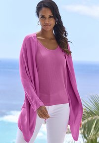 Lichtgewicht roze cardigan en tanktop in een gestructureerde breiwerk, gecombineerd met witte broeken; lange mouwen met een open, vloeiende ontwerp, relaxte pasvorm.