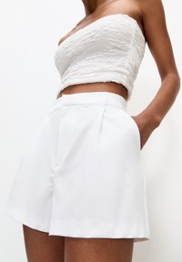 Short blanc avec une coupe ajustée, présentant un devant plat, des poches latérales et une texture lisse. Le tissu semble léger et structuré.