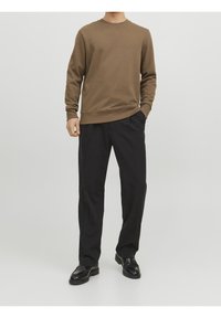 Maglione di cotone marrone con collo a giro, maniche a coste, abbinato a pantaloni neri sartoriali con gamba dritta e tasche laterali, indossato con scarpe nere.