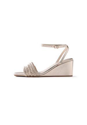 Sandalo beige con zeppa con cinturino intrecciato anteriore e sottile cinturino alla caviglia con fibbia su sfondo bianco.