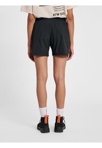 Czarne szorty z elastycznym pasem, wykonane z lekkiego materiału. Połączone z czarnym obuwiem z pomarańczowymi akcentami i białymi skarpetkami.
