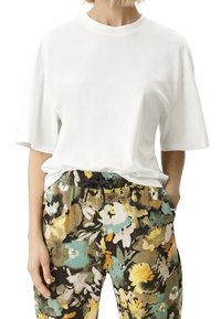 Biały bawełniany t-shirt w zestawieniu z czarnymi spodniami w kwiatowy wzór z żółtymi, zielonymi i kremowymi akcentami oraz ze sznurkiem w pasie.