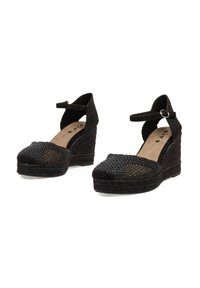 Sandalias de cuña negras con textura tejida, punta abierta, tira de tobillo con hebilla y base de tacón sólida.
