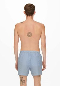 Bañador de rayas azul y blanco con cintura elástica, que cuenta con un bolsillo trasero y un tejido transpirable. Tatuaje visible en la parte posterior.